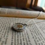 White daisy flower pendant necklace with silver chain lying on a book page