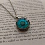 Blue pressed daisy pendant necklace displayed on book text