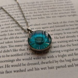Blue pressed daisy pendant necklace displayed on book text