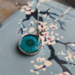 Blue pressed daisy pendant necklace displayed on book text