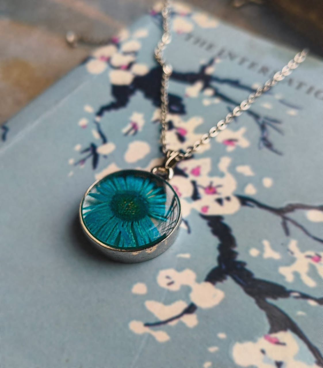Blue pressed daisy pendant necklace displayed on book text